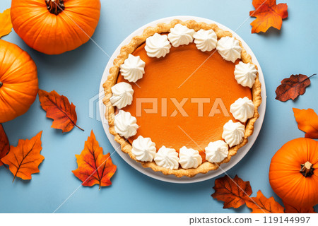 Closeup of pumpkin pie with dollops of whipped cream and sprinkle of cinnamon on white plate and fall holiday background 119144997