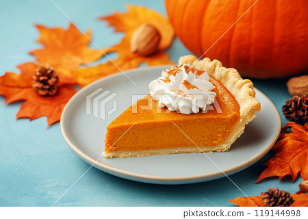 Closeup of pumpkin pie slice with dollops of whipped cream and sprinkle of cinnamon on plate and fall holiday background 119144998