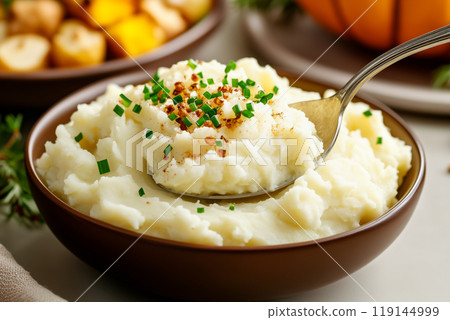 Bowl filled with mashed potatoes topped with butter with spoon on holiday background. Thanksgiving Day side dishes 119144999