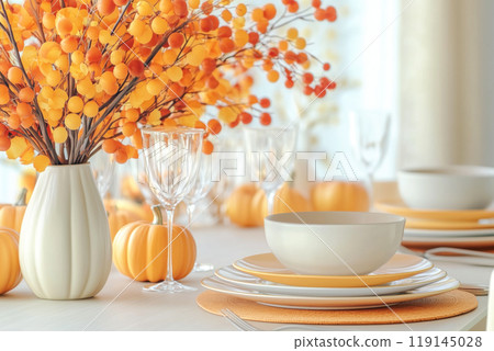Autumn table setting with bowls, plates, wine glasses, pumpkins and floral centerpiece in vase on soft focus background. 119145028