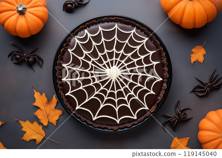 Chocolate tart with spider web design and spider decoration on black background. Concept of Halloween dessert 119145040