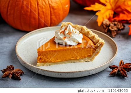 Closeup of pumpkin pie slice with dollops of whipped cream and sprinkle of cinnamon on plate and fall holiday background Closeup of pumpkin pie slice with dollops of whipped cream and sprinkle of cinnamon on plate and fall holiday background 119145063