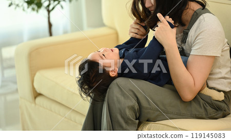 Joyful mother playing with laughing baby boy lying on her legs. Family, tenderness and parenthood concept Joyful mother playing with laughing baby boy lying on her legs. Family, tenderness and parenthood concept 119145083