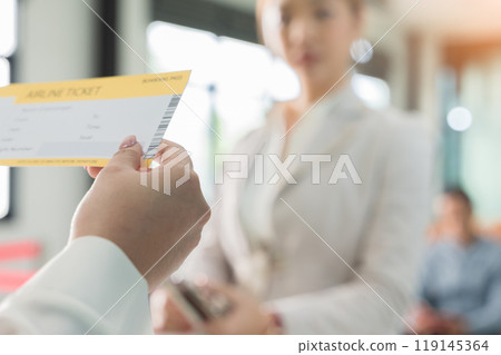Airline attendant female hand holding airline boarding ticket in front of blurred woman passenger at airport check in counter 119145364