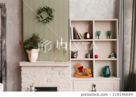 Beige fireplace mantel with christmas wreath and wooden rocking horse in living room 119146684