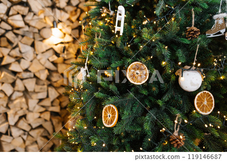 Christmas tree with orange decorations and lights, surrounded by a pile of wood 119146687