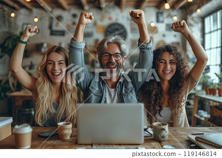 Business team are smiling and holding up their hands in the air, with a laptop in front of them. Scene is happy and celebratory 119146814