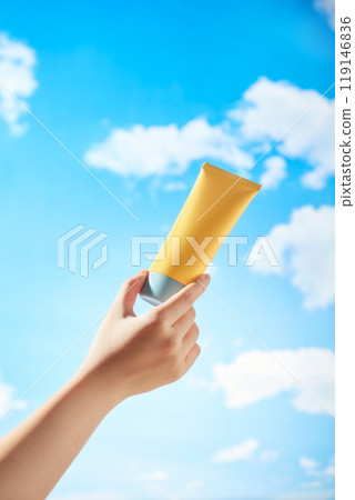 A mockup yellow cream tube is being held by a female model against a clear blue sky with white clouds drifting by. Minimalist image used for advertisements of skincare products. 119146836