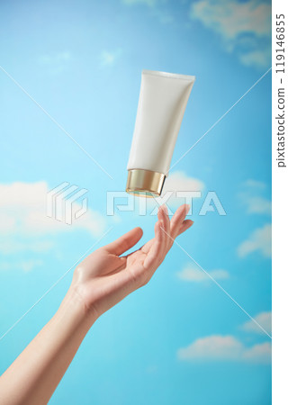 A female model is shown catching for an unmarked white tube of cream in the sample photograph used to promote the skin care product. The image is set against a gorgeous blue sky with drifting clouds. A female model is shown catching for an unmarked white tube of cream in the sample photograph used to promote the skin care product. The image is set against a gorgeous blue sky with drifting clouds. 119146855