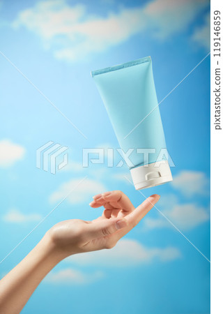 A female model hand is gently preparing to touch an unbranded blue cream tube with a white cap floating in the bright blue sky, a sample image for skincare advertisements. A female model hand is gently preparing to touch an unbranded blue cream tube with a white cap floating in the bright blue sky, a sample image for skincare advertisements. 119146859