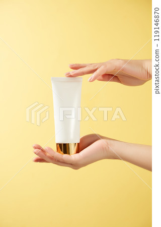 In the promotional shot for the skincare product, a female model is holding an unlabeled white tube of cream in her hand. The backdrop of the photograph is bright yellow. 119146870
