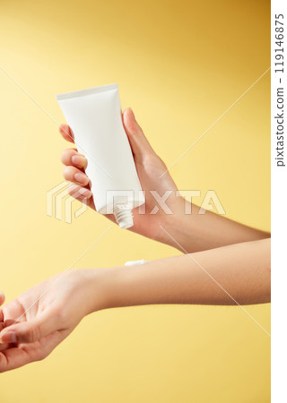 Perfect for sunscreen advertising, this minimalist image shows a model applying an unlabeled white tube of cream to her wrist against a brilliant orange background that mimics the sun. 119146875