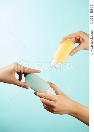 Pictured on a vivid blue backdrop are two hands holding a blue and a yellow lotion bottle. The image has an element of freshness, making it suitable for a skincare campaign. 119146898