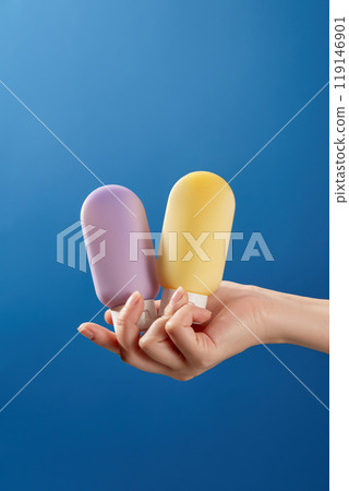 Minimalist image layout for skincare product advertisement on a dark blue background resembling the sky with a hand holding the cap of the same cream tube mockup without purple and yellow label. 119146901