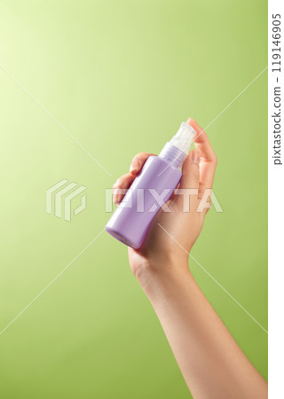 The image used as a template for product advertisements shows a serene green background with a woman hand delicately grasping a unlabeled purple spray bottle, sample image for skincare advertisement The image used as a template for product advertisements shows a serene green background with a woman hand delicately grasping a unlabeled purple spray bottle, sample image for skincare advertisement 119146905