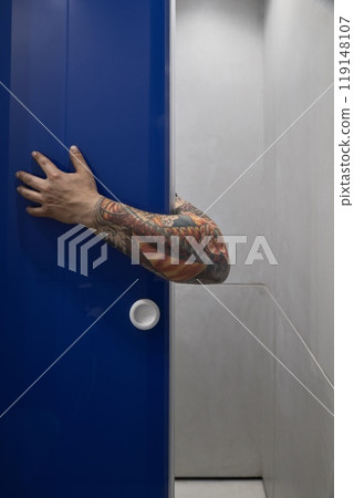An intriguing arm emerges from a blue door in a contemporary space, captivating viewers 119148107