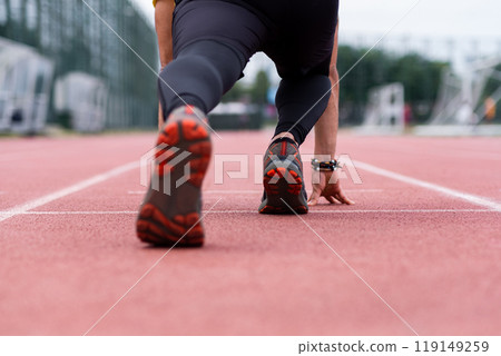 Close-up view of a runner's legs, primed in a low start position, signaling the beginning of an energetic sprint along the urban outdoor stadium's red rubberized track.  119149259
