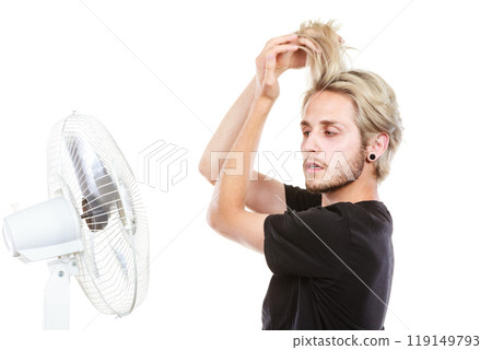 Young man fighting with wind from cooling fan Young man fighting with wind from cooling fan 119149793