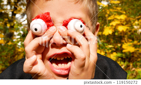 A boy in a Halloween costume puts the scary plastic eyes of a dead man to his eyes and scares all. A boy in a Halloween costume puts the scary plastic eyes of a dead man to his eyes and scares all. 119150272