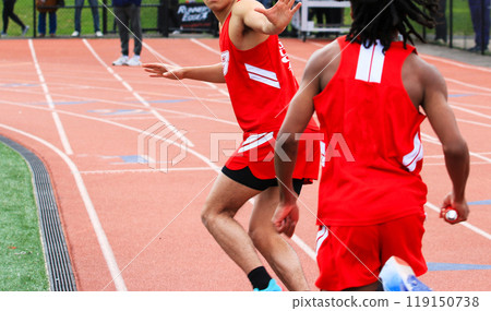 Runners exchanging the baton during a track relay race outdoors 119150738