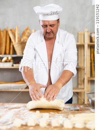 Male baker in unbuttoned uniform prepares dough, kneads it with his hands 119151242