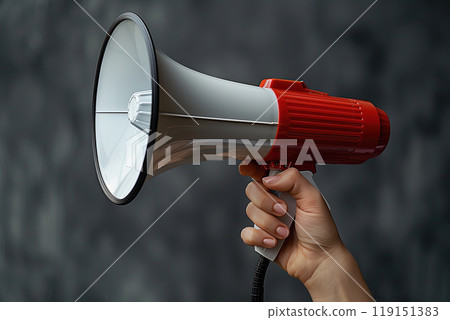 A close-up image of a person's hand holding a red and white megaphone against a dark background 119151383