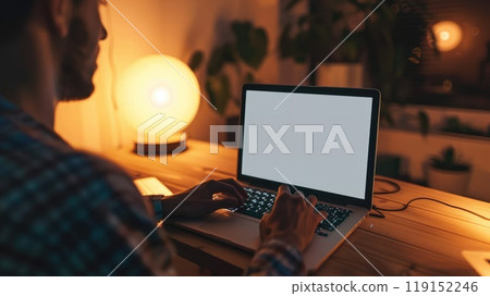 A man is typing on a laptop in a dimly lit room 119152246