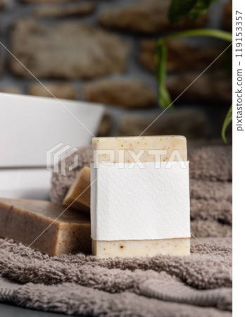 Soap bar with blank label on brown folded towels near plant and basin in bathroom, mockup 119153357