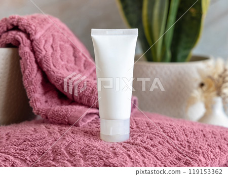 White cream tube on pink towels near green plant close up in bathroom, cosmetic mockup White cream tube on pink towels near green plant close up in bathroom, cosmetic mockup 119153362