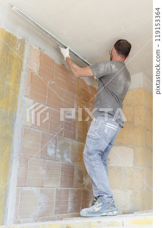 Craftsman in dirty gloves and gray shirt checking the ceiling surface with straight edge Craftsman in dirty gloves and gray shirt checking the ceiling surface with straight edge 119153364