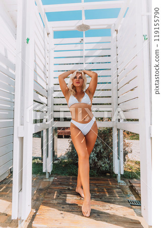 A woman in a bikini stands in front of a white shower stall. She is smiling and she is enjoying the moment A woman in a bikini stands in front of a white shower stall. She is smiling and she is enjoying the moment 119155790