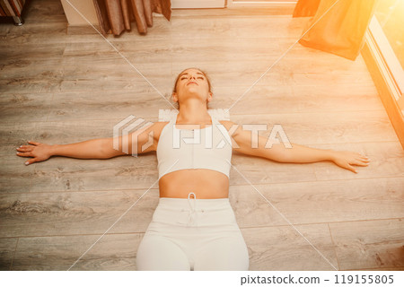 Adult athletic woman, in white bodysuit, performing fascia exercises on the floor - caucasian woman using a massage foam roller - a tool to relieve tension in the back and relieve muscle pain - the 119155805