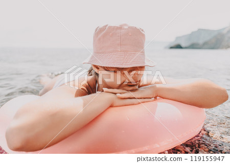 A woman is laying on a pink inflatable raft in the ocean. She is wearing a pink hat and a white bikini. A woman is laying on a pink inflatable raft in the ocean. She is wearing a pink hat and a white bikini. 119155947
