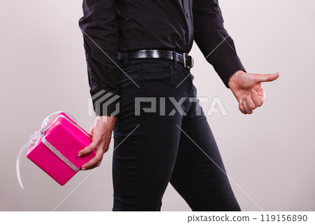 Man hiding pink gift box with ribbon behind back Man hiding pink gift box with ribbon behind back 119156890