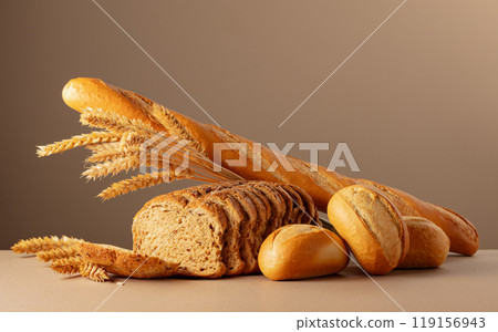 Sliced bread, baguette, and French buns with wheat ears on a beige background. Sliced bread, baguette, and French buns with wheat ears on a beige background. 119156943