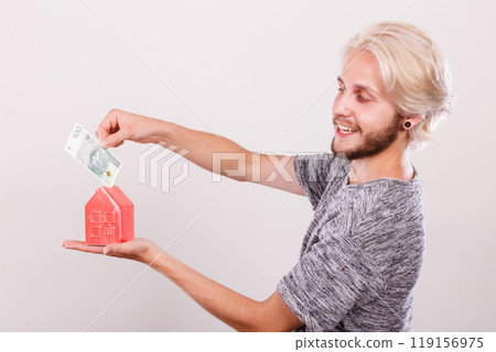 Man putting money into house piggybank 119156975