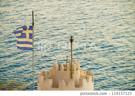Little church with greek flag on rocky seashore 119157125