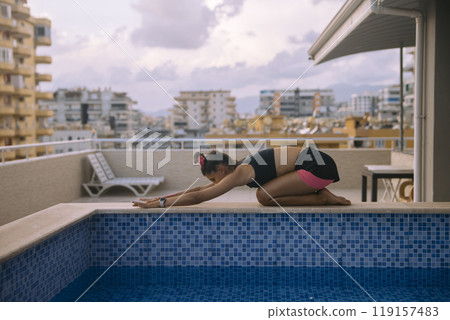 Engaging in a Relaxing Yoga Pose by the Poolside while enjoying the Urban Setting around you Engaging in a Relaxing Yoga Pose by the Poolside while enjoying the Urban Setting around you 119157483