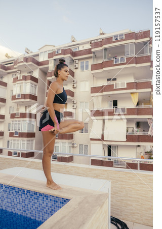 A young woman practices yoga by a beautiful pool on a bright, energetic, sunny day A young woman practices yoga by a beautiful pool on a bright, energetic, sunny day 119157537