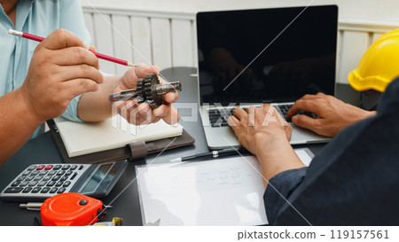 The engineering team point to the gear and discussing on their project together. The engineering team point to the gear and discussing on their project together. 119157561