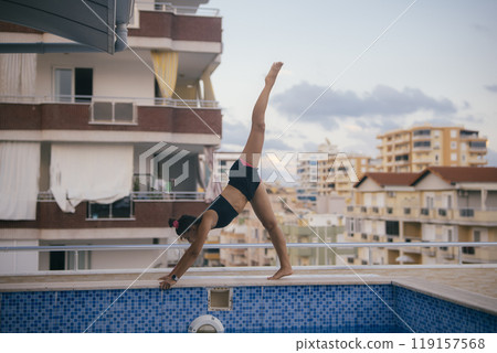 A highly skilled gymnast executes a truly impressive handstand at the poolside during dusk A highly skilled gymnast executes a truly impressive handstand at the poolside during dusk 119157568