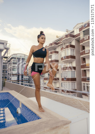 Woman Engaged in Practicing Balance by the Poolside While Surrounded by an Urban Setting 119157571