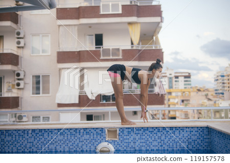 A Young Woman is Actively Preparing for a Dive by the Poolside at a Modern Apartment Complex A Young Woman is Actively Preparing for a Dive by the Poolside at a Modern Apartment Complex 119157578