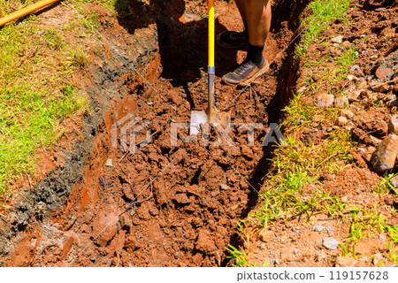 Worker digs trench with shovel for drainage pipe at construction site 119157628