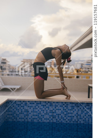 Dynamic Yoga Pose Practiced at Poolside Against a Beautiful and Scenic Sky Above Dynamic Yoga Pose Practiced at Poolside Against a Beautiful and Scenic Sky Above 119157681
