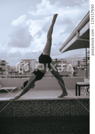 A Woman Engaged in Performing a Yoga Pose on a Rooftop with a Beautiful Urban Background A Woman Engaged in Performing a Yoga Pose on a Rooftop with a Beautiful Urban Background 119157690
