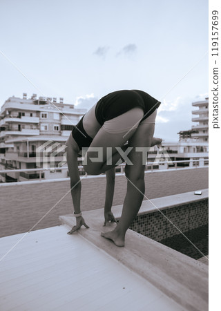 Engaging in a Dynamic Yoga Pose on a Rooftop with a Stunning Urban Background Setting 119157699