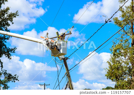 Using utility tower truck, emergency service linemen repair power electrical lines damaged by storm hurricane Using utility tower truck, emergency service linemen repair power electrical lines damaged by storm hurricane 119157707
