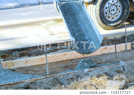 Concrete mixer pours fresh concrete on reinforced bars for new sidewalk Concrete mixer pours fresh concrete on reinforced bars for new sidewalk 119157727