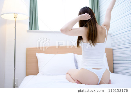 一位身穿內衣的年輕苗條女子醒來後，沐浴在早晨的陽光下，在臥室裡伸展身體。 119158176